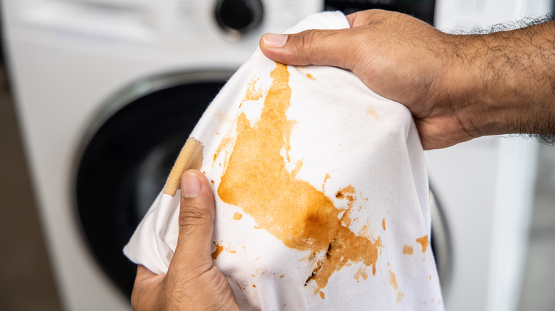 man holding white shirt with coffee stain in front of washing machine