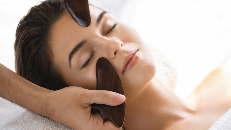 Woman getting facial massage with gua sha 