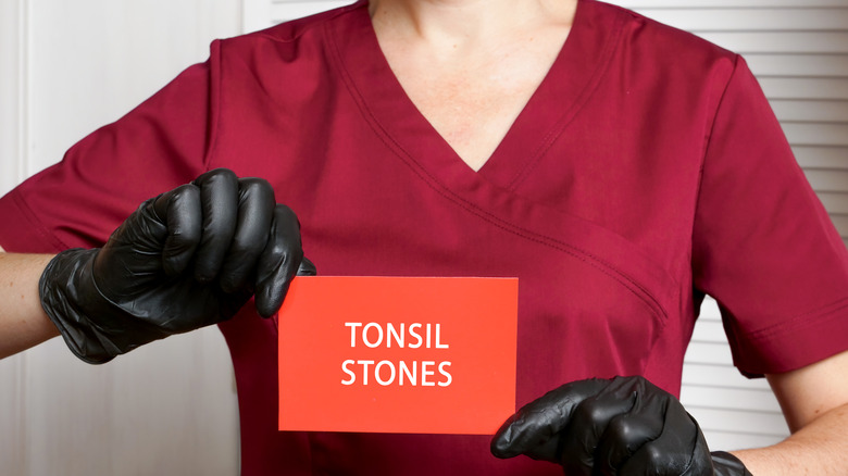 Woman with gloves holding a "tonsil stones" sign