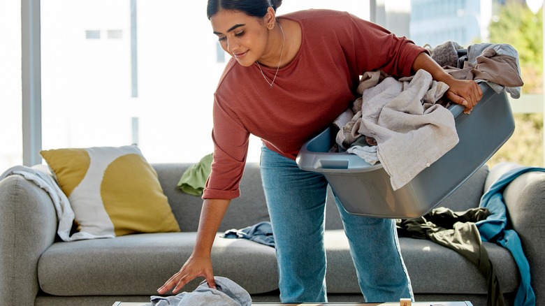 Woman picking up clothes, holding laundry basket