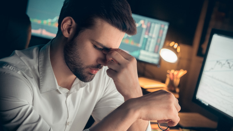 man rubbing eyes while working computers