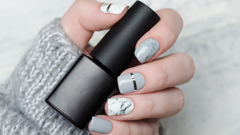 square manicure with grey marble polish holding a black pot of nail varnish