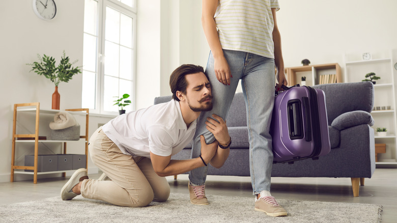 Man grabs woman's leg walking away holding suitcase