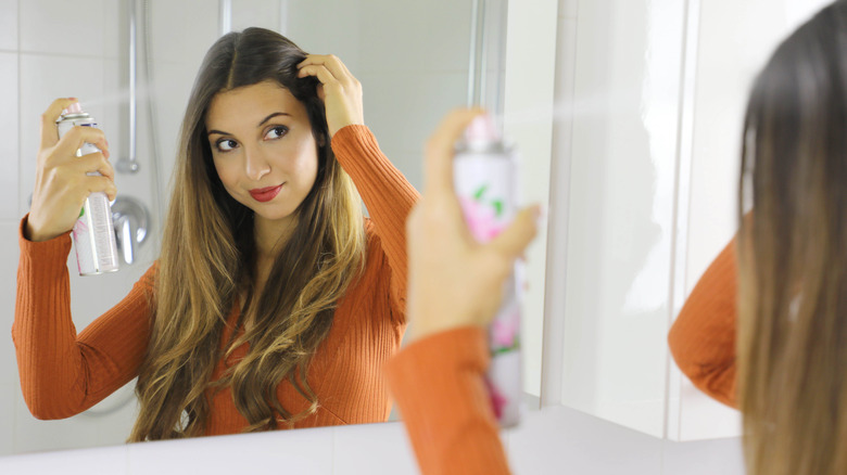 A woman applies dry shampoo to her hair.