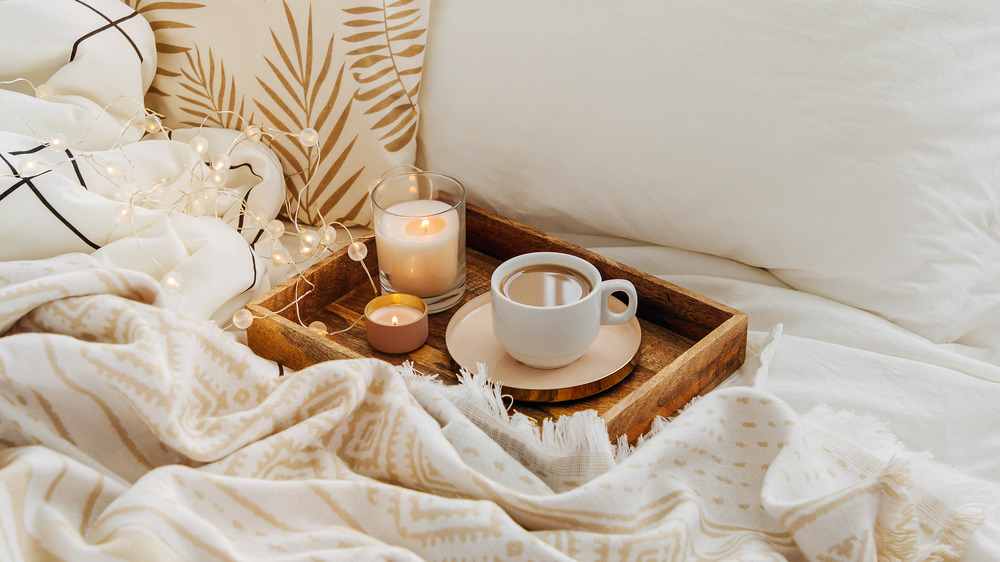 Cozy bedding and tray with coffee cup and candles