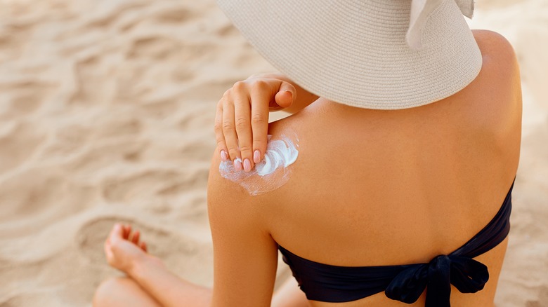 woman in hat applying sunscreen