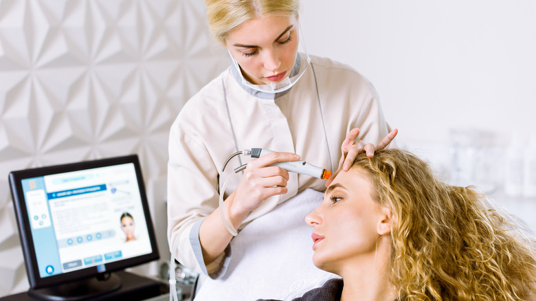 Blonde woman receiving a HydraFacial from a technician.