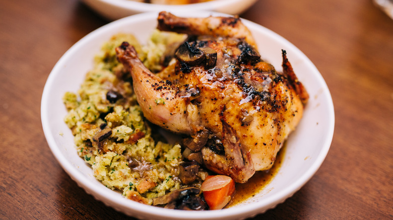 Roasted Cornish Game Hen with Stuffing served in a Shallow White Dish on a Wood Table