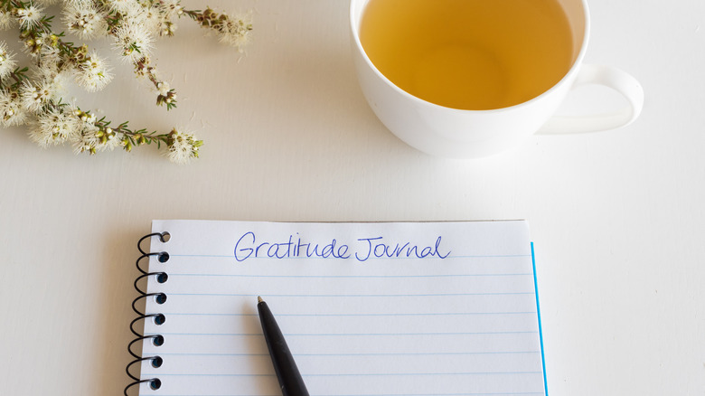 Gratitude Journal notebook and pen on table with cup of tea and flowers