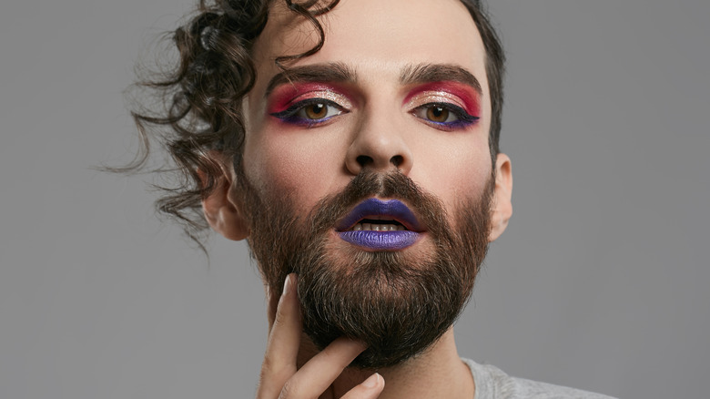 A person wears bold eyeshadow and a purple lip