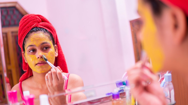 Young woman applying a turmeric mask for acne cysts