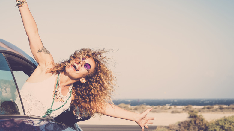 Woman with curly hair hanging out a car window