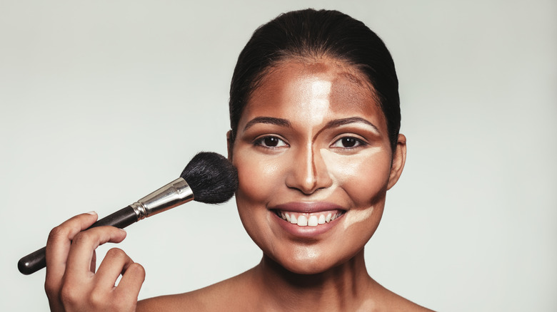 A woman applying contour to her face with a brush