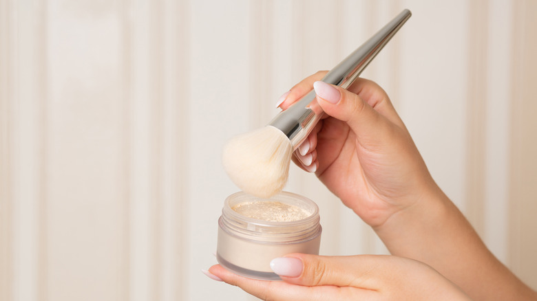 A hand holding a brush and compact full of powder