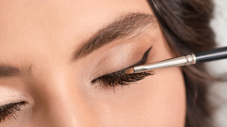 a woman with her eyes closed, applying eyeliner to her eyelid