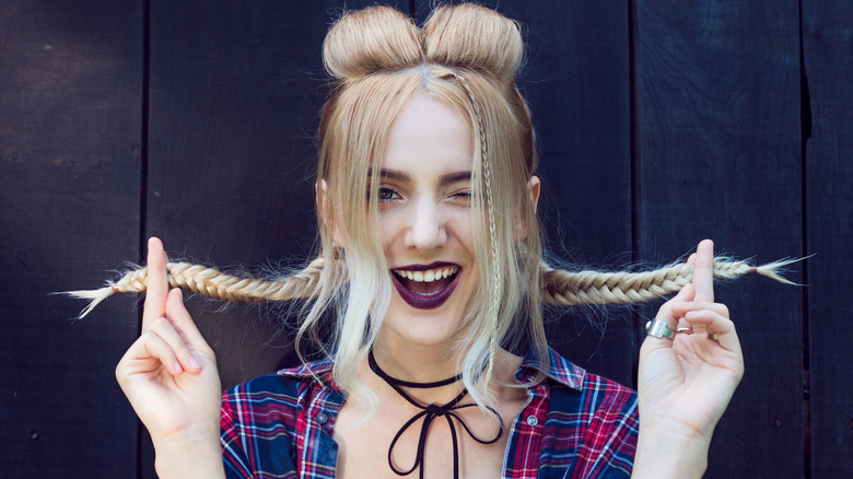 Woman holds her braids and winks