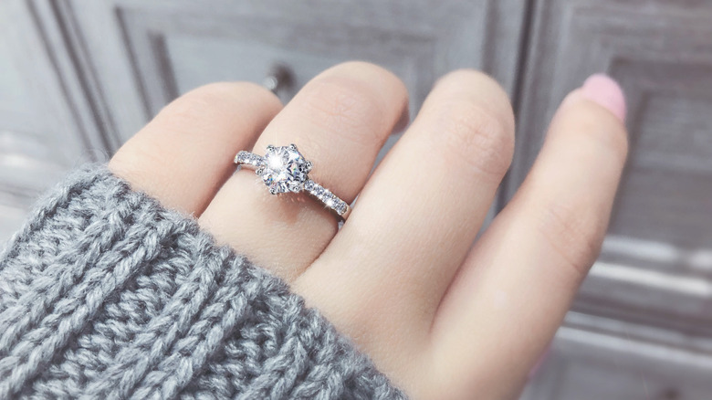 A woman wearing a gray sweater and showing her engagement ring 