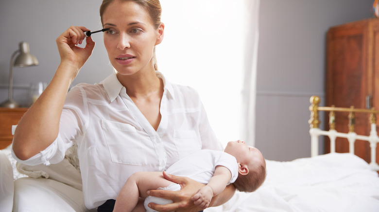 Woman applying mascara while holding a baby