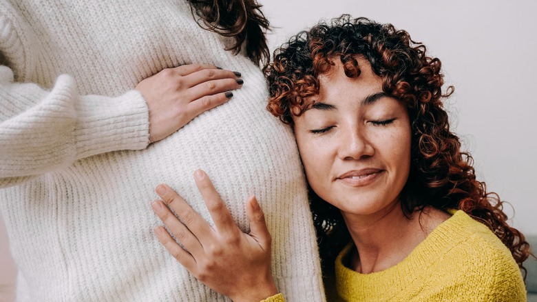 Woman putting her ear against partner's pregnant belly