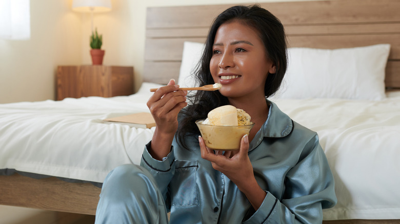 A woman eating ice cream in her bedroom