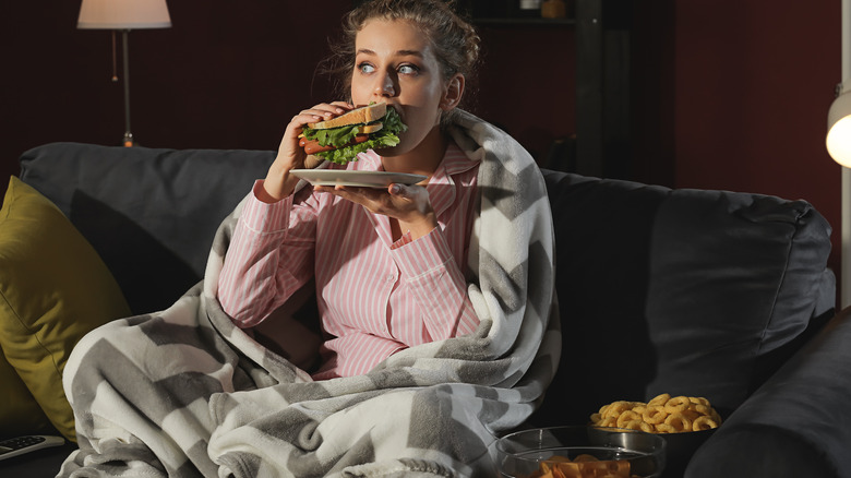 Woman eating sandwich watching TV