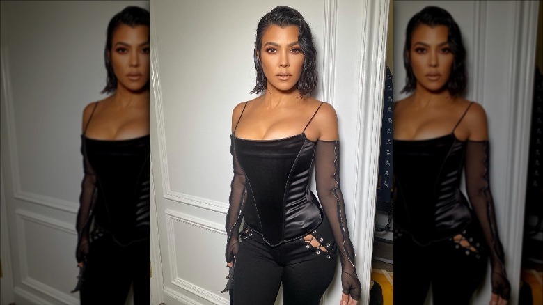 Kourtney Kardashian posing in a corset top and tie-up black pants