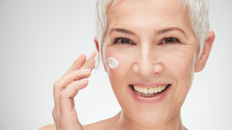 Grey-haired woman using moisturizer