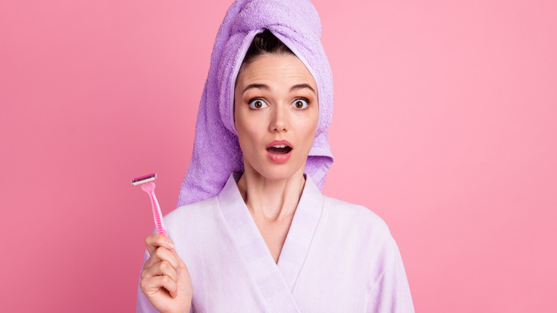 woman wearing purple towel & robe looks surprised holding razor