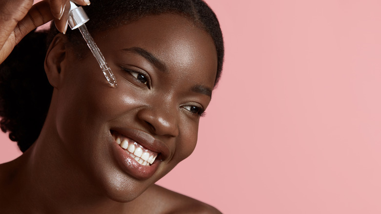 Woman smiling while applying skin serum