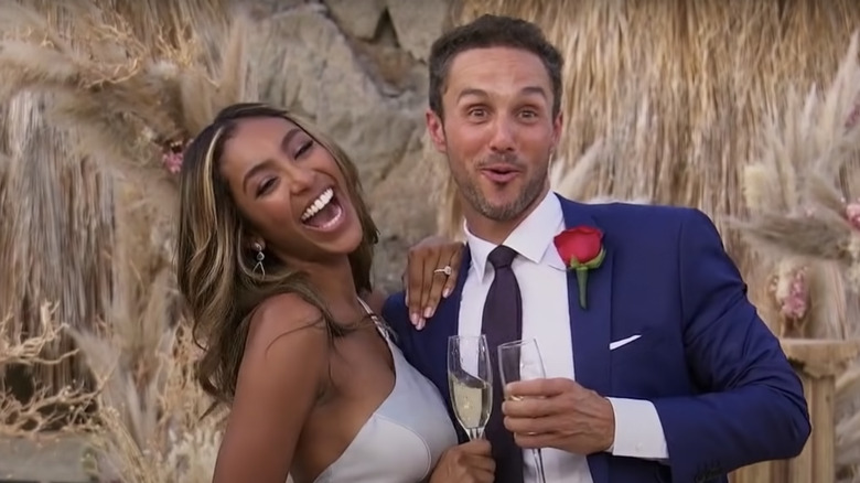 Tayshia and Zac smiling with champagne