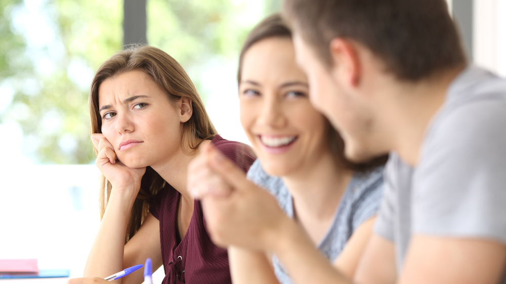 Woman looking unhappy as other woman and man talk