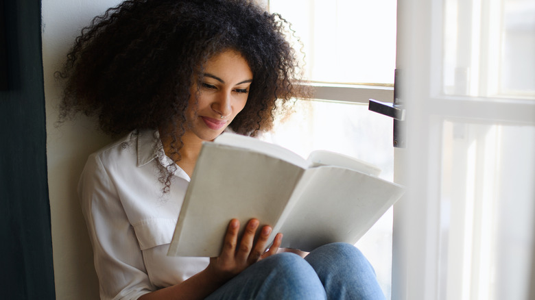 A young woman reads a book by a window