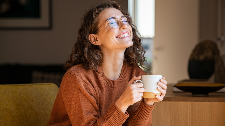 A woman smiling, holding a cup of coffee 