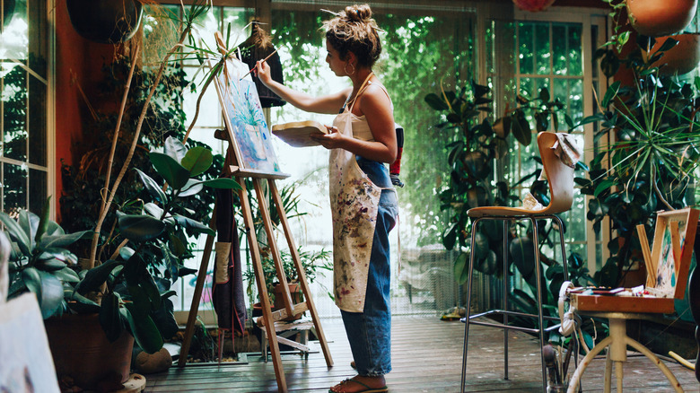 Woman painting in her greenhouse filled with plants