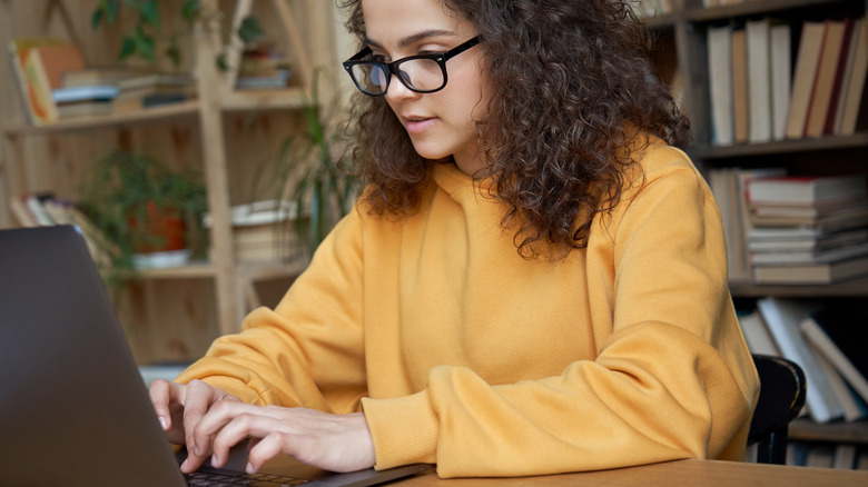 Woman typing on her laptop in front of her bookcase