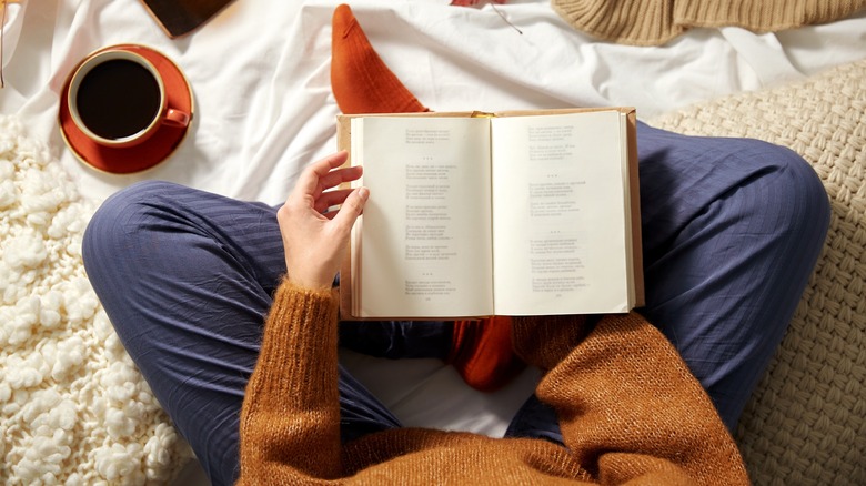 Cross-legged person holding open book with coffee nearby