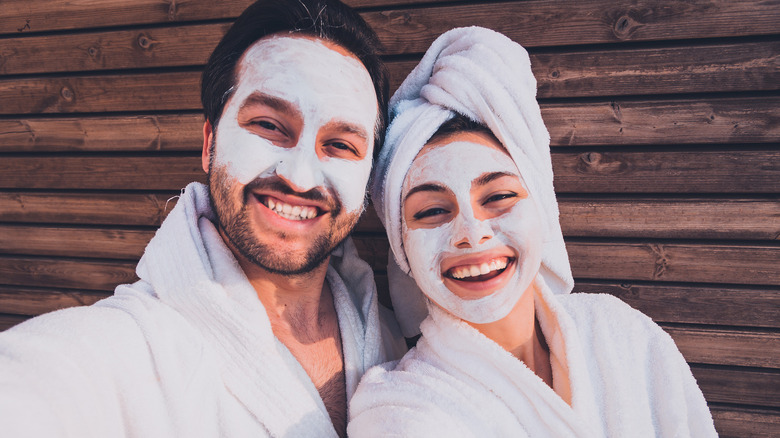 Couple takes a selfie with clay face masks and robes