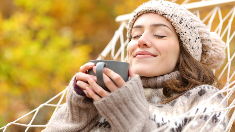 A woman smiling in a hammock, holding a mug 