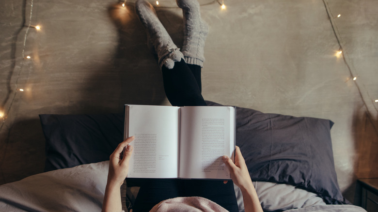 woman laying on a bed holding up a book