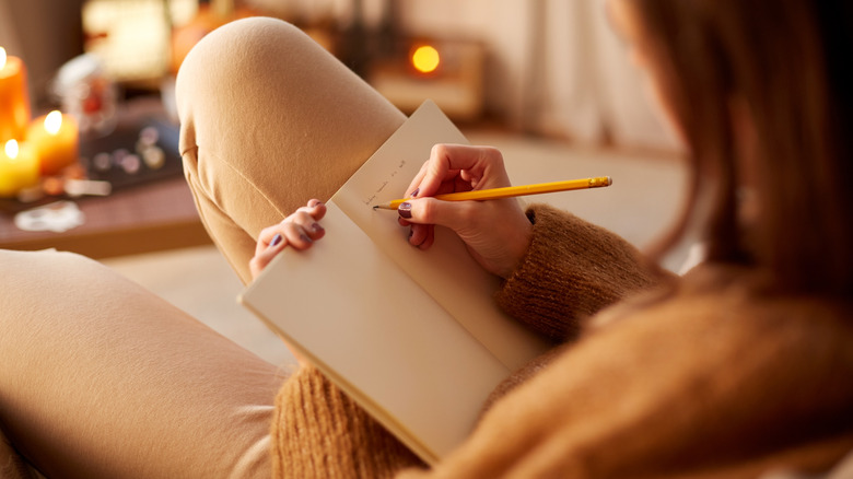 Someone writing in a journal with candles lit in the background