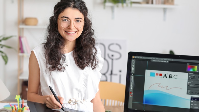 woman with glasses and stylus smiling by computer