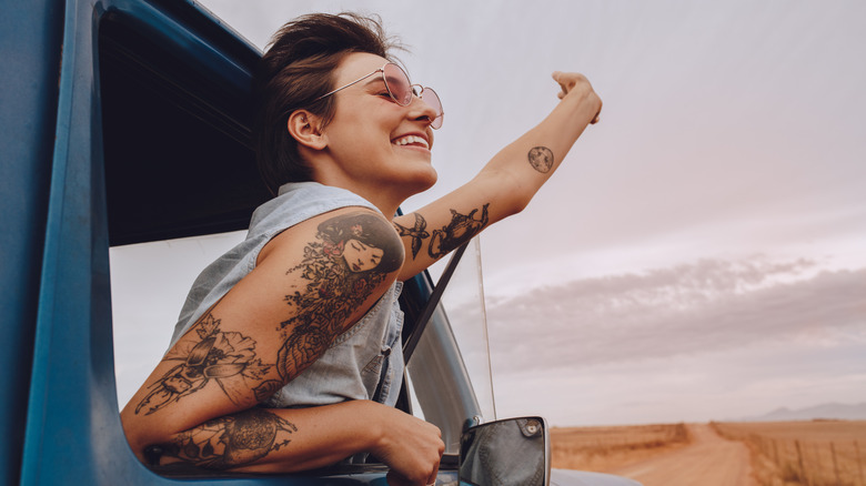 Woman with tattoos hanging outside a car window, road trip