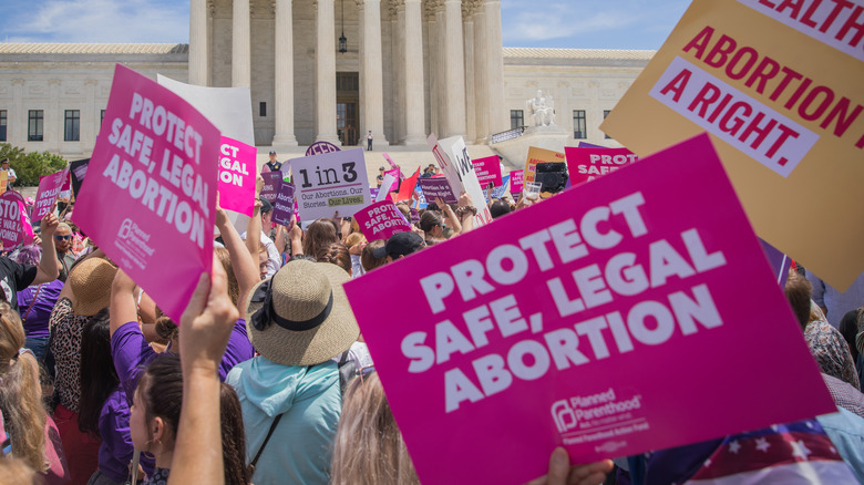 protestors at a pro abortionr ally holding sayings saying "protest safe, legal abortion"