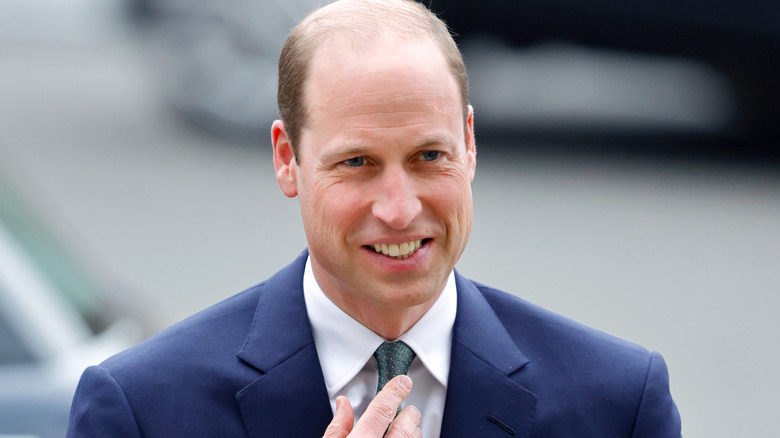 Prince William straightening his tie and smiling