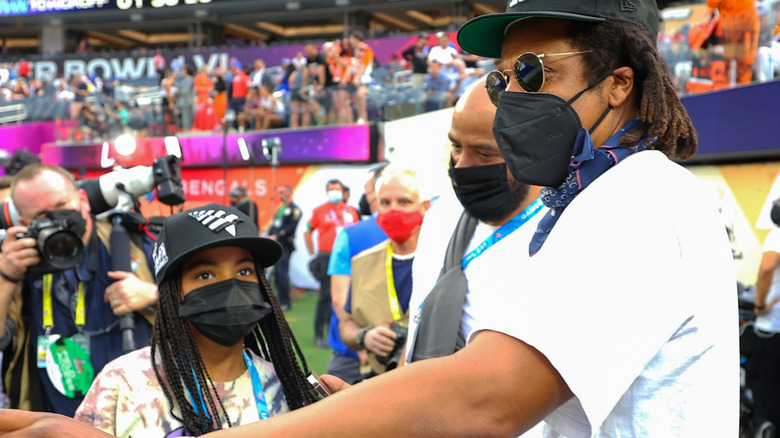 Blue Ivy and Jay-Z standing on sidelines at sports event