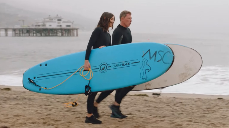 Sophie Flay and Bobby Flay carrying their surfboards