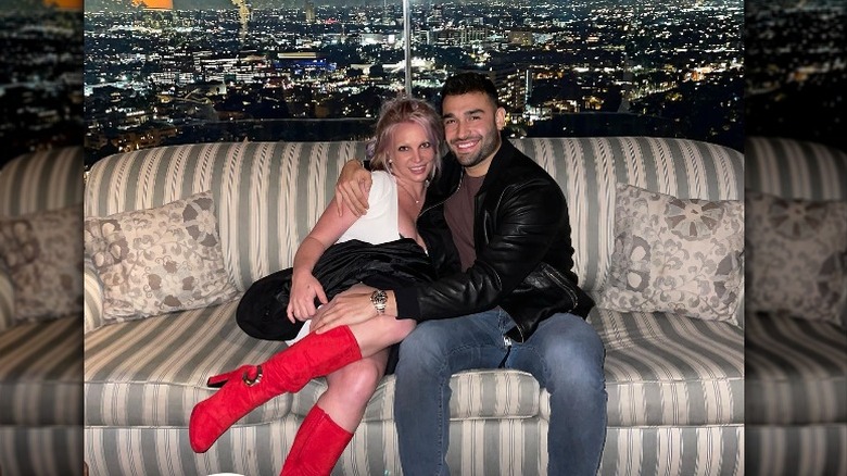 Britney Spears and Sam Asghari, cuddling on couch with city in background