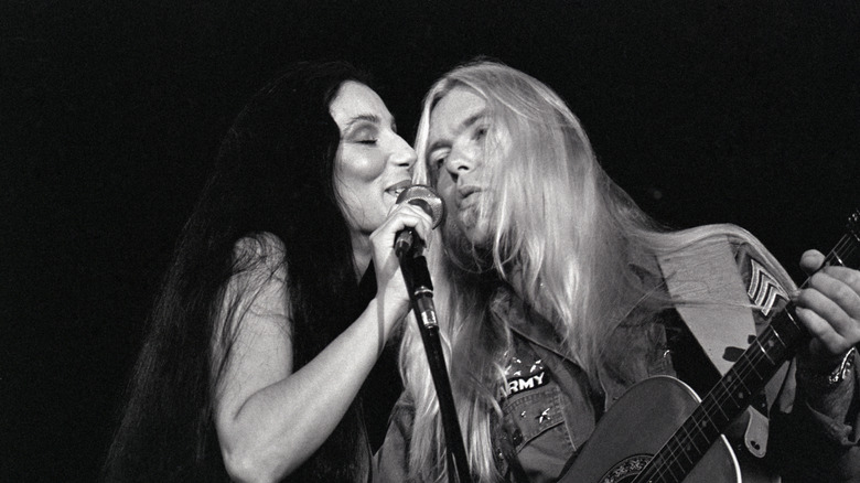 Cher and Gregg Allman singing into microphone