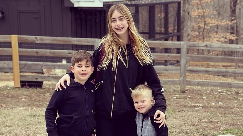 Taylor Hall stands smiling with arms around her younger brothers