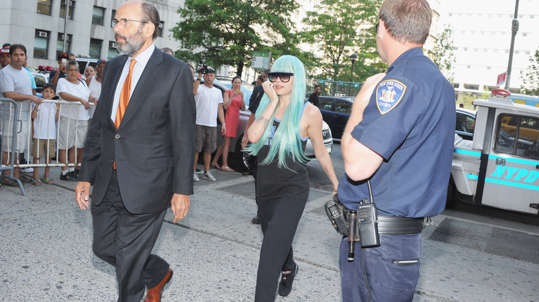 Amanda Bynes in green wig walking with lawyer and police